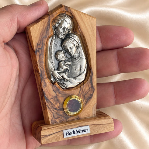 Hand holding a Holy Family olive wood plaque, showing its compact size and natural wood grain