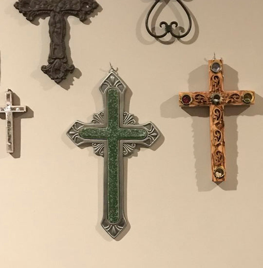 Variety of Latin crosses in different colours, made of wood and iron, hanging on a white wall.