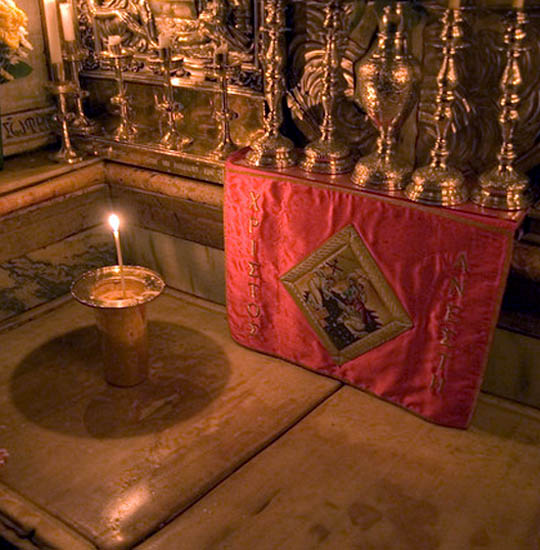 A marble slab placed over the tomb of Jesus Christ with candles and relics around it.