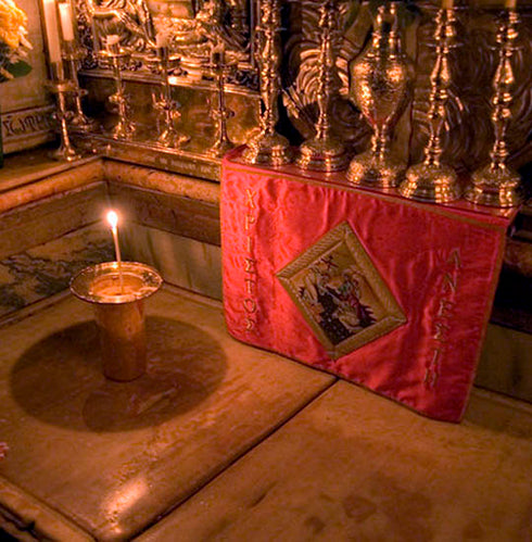 A marble slab placed over the tomb of Jesus Christ with candles and relics around it.