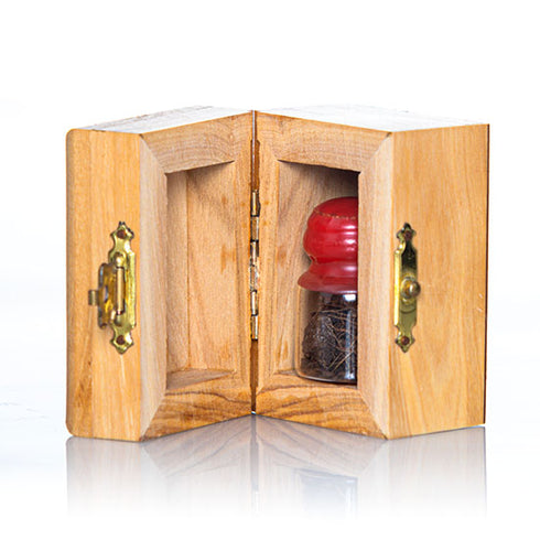 A small handcrafted olive wood box against white background, with a glass vial and red cap inside, containing holy soil from Jerusalem.