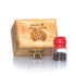 A handcrafted olive wood box with a glass vial containing holy soil, and a red cap on top. The box has engraved text 'PIECE OF HOLY LAND'.
