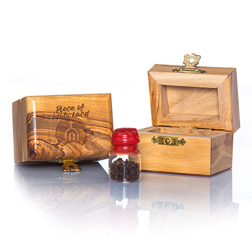 Two small Piece of Holy Land handcrafted olive wood boxes against white background, accompanied by a glass vial with red cap next to it, containing holy soil from the Holy Land.