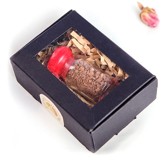 A glass vial containing sacred soil from Jerusalem, sealed with a red cap, placed inside a black box with a clear window showing the vial.