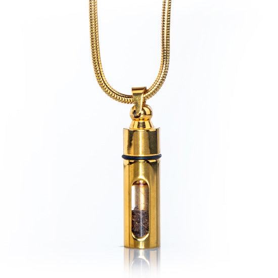 Golden stainless steel pendant with a clear glass section containing Holy Soil on white background