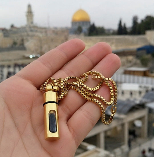 Gold whistle with chain held in a hand, with a blurred background of a cityscape.