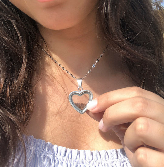 Person wearing a silver heart-shaped necklace with a hand adjusting it.