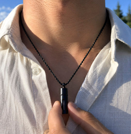 Person wearing a black necklace with a pendant, outdoors.
