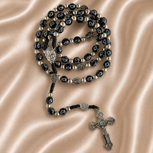 Black bead rosary with silver accents, Virgin Mary and Jerusalem Cross medals, and ornate silver crucifix on satin fabric