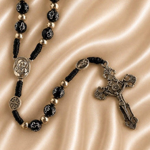 Close-up of black bead rosary with Virgin Mary medal, Jerusalem Cross medal, and ornate silver crucifix on satin fabric