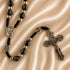 Close-up of black bead rosary with Virgin Mary medal, Jerusalem Cross medal, and ornate silver crucifix on satin fabric