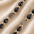 Close-up of black rosary beads with silver spacers, Virgin Mary and Jerusalem Cross medals on satin fabric background