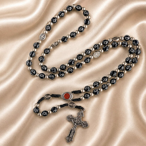 Black bead rosary with silver accents, red Holy Soil centerpiece, and silver crucifix on a satin fabric background