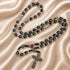 Black bead rosary with silver accents, red Holy Soil centerpiece, and silver crucifix on a satin fabric background