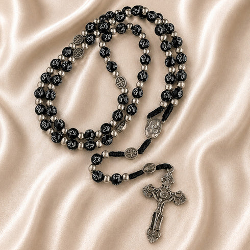 Black bead rosary with silver accents, devotional medals, and silver crucifix on a satin fabric background