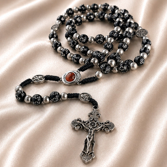 Black bead rosary with silver accents, Holy Soil centerpiece, and ornate silver crucifix on a satin cloth