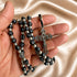 Hand holding a black bead rosary with silver accents, devotional medals, and ornate silver crucifix