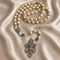 White and gold rosary with cross-pattern beads and ornate silver crucifix on a champagne satin fabric background.