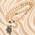 White and gold rosary with cross-pattern beads, medals, a Jerusalem soil centerpiece, and an ornate silver crucifix
