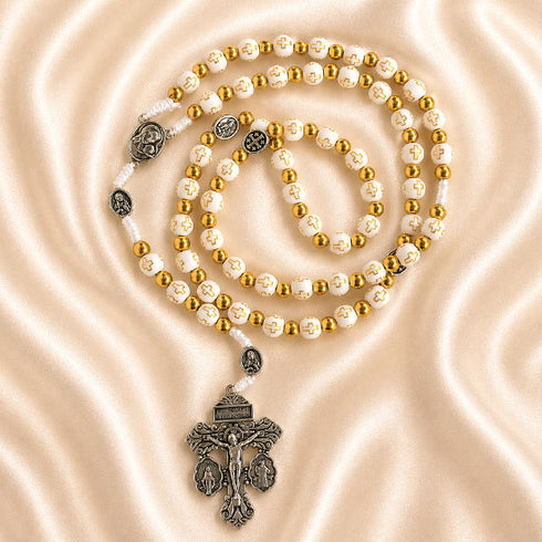 White and gold rosary with cross-pattern beads, devotional medals, and an ornate silver crucifix on a satin fabric.