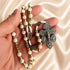 Hand holding a white and gold rosary with cross-pattern beads, a Jerusalem soil centerpiece, devotional medals, and a silver crucifix