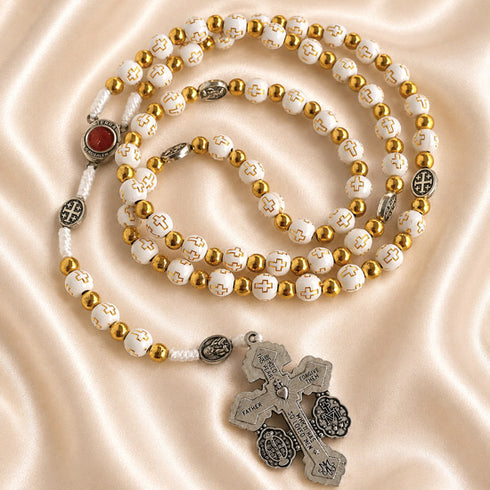 White rosary with Holy Soil centerpiece, Jerusalem cross medals, and silver crucifix on a satin fabric background