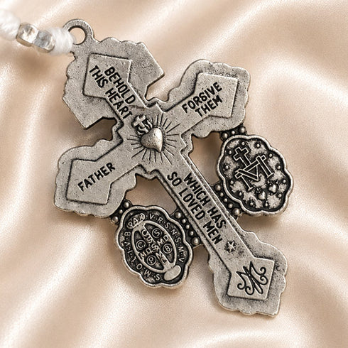 Close-up of an ornate silver crucifix with St. Benedict and Marian medals on a champagne satin fabric background.