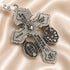Close-up of an ornate silver crucifix with St. Benedict and Marian medals on a champagne satin fabric background.