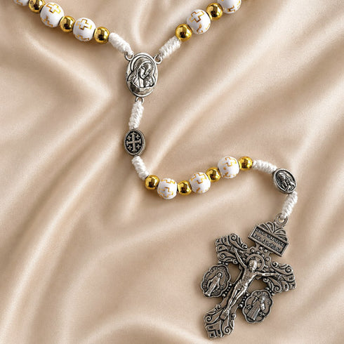 White and gold rosary with Virgin Mary centerpiece, Jerusalem Cross medal, and ornate crucifix on champagne satin.
