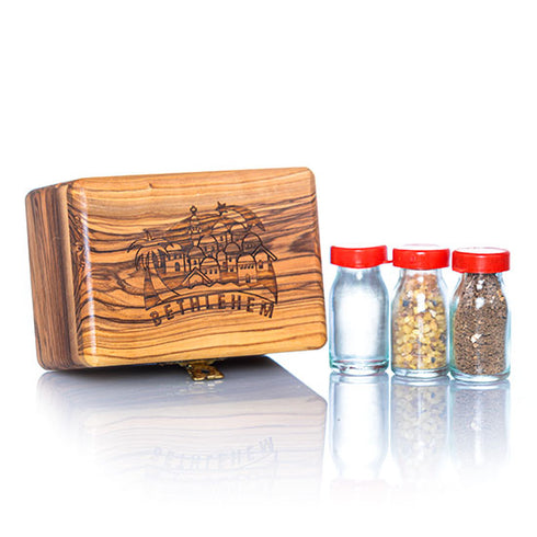 A handcrafted olive wood box against white background, with a design that includes a Bethlehem Star and panorama and the word 'Bethlehem' on the lid, accompanied by three glass vials with red caps next to it, containing holy water, incense, and holy soil.