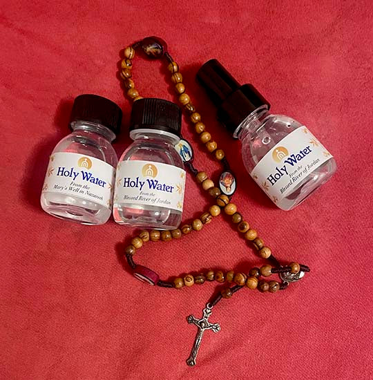 Olive wood rosary and three 60ml vials of Holy Water on a red cloth.