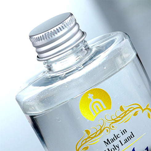 Top detail of A clear plastic bottle containing Holy Water from the Holy Land, with a metal cap and a label featuring gold, blue and black text, and a graphic symbol.
