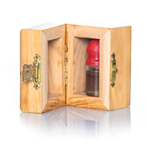 A small handcrafted olive wood box against white background, accompanied by a glass vial with red cap inside, containing holy water from the Jordan River.