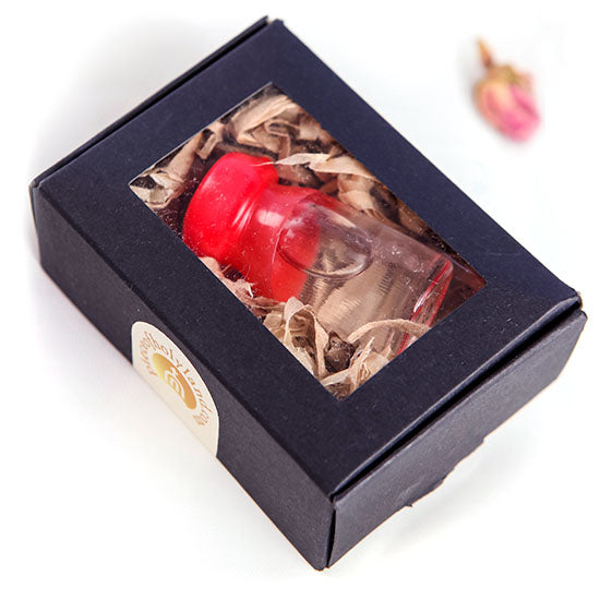 A glass vial containing Holy Water from the Jordan River, presented in a black paper box with a red cap and a white background.