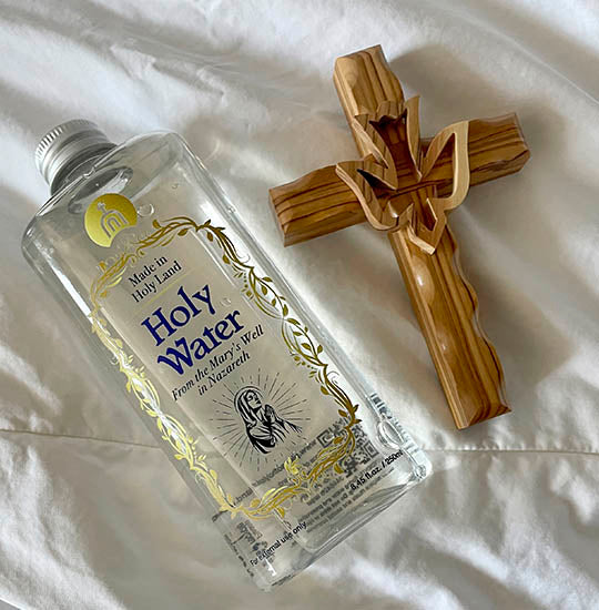 Plastic bottle of the Holy Water from Mary's Well and an olive wood cross next to it.