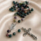 A rosary with multicolored stone beads, a silver-tone medallion, and a silver-tone crucifix, on draped satin fabric.