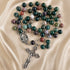A rosary with polished green, purple, red, and white marbled beads, silver-tone chain links, a round medallion, and a detailed crucifix.