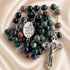 A multicolor gemstone rosary with beads in shades of green, purple, brown, and gray, a silver-tone crucifix and a medallion.