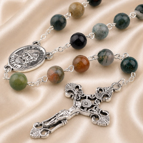 A rosary with beads in green, black, brown, and gray, silver-tone chain links, an oval Saint Charbel medal, and an ornate crucifix.