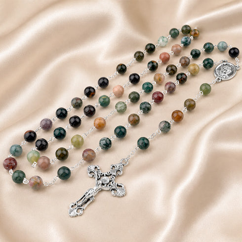 A multicolor rosary with silver-tone metal links, polished beads and a silver crucifix, on a draped beige satin fabric.