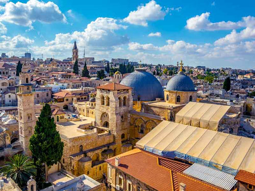 Arial view of golden cross shining over the blue dome of the Church of the Holy Sepulchre rooftop, on a sunny day.