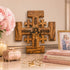 Wooden cross with religious text, books, and flowers on a table.