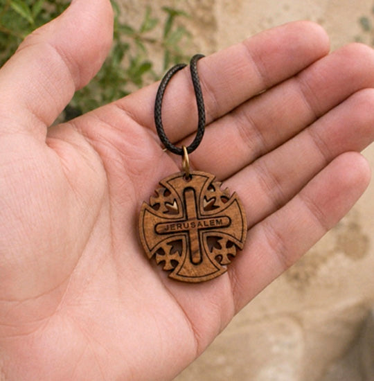 Hand holding a Jerusalem cross pendant on a leather cord