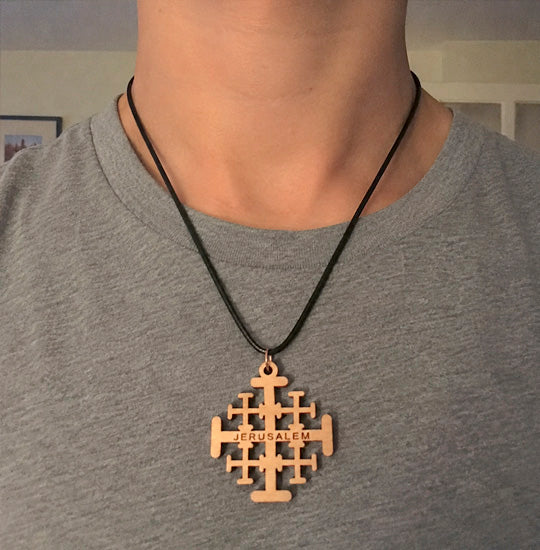 Person wearing a necklace with a Jerusalem cross pendant on a plain background