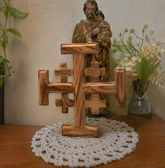 Wooden sculpture of a religious figure holding a child on a table with a cross and flowers.