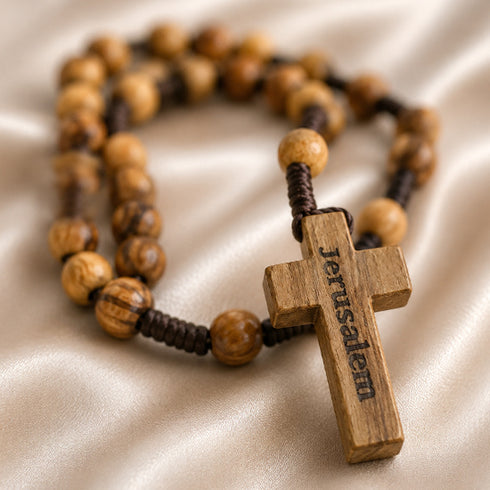 Olive wood rosary with cord and a wooden cross with Jerusalem written on it, on a beige background.