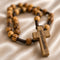 Olive wood rosary with cord and a wooden cross with Jerusalem written on it, on a beige background.
