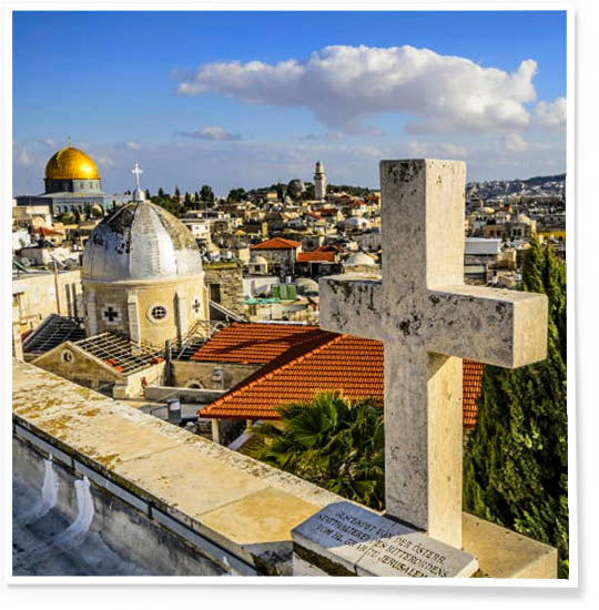 Panoramic view of the rooftops of Jerusalem’s Old City, showcasing historic architecture and religious landmarks and a stone cross under a bright sky.