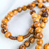 Close up on the beads of an olive wood rosary, laid out on a clean white surface.