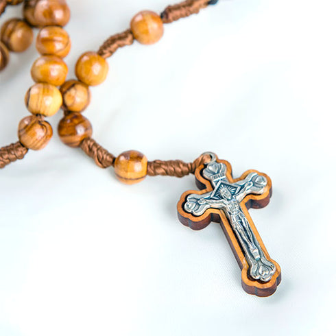 Close up image of a handmade olive wood rosary featuring crucifix, laid out on a clean white surface.